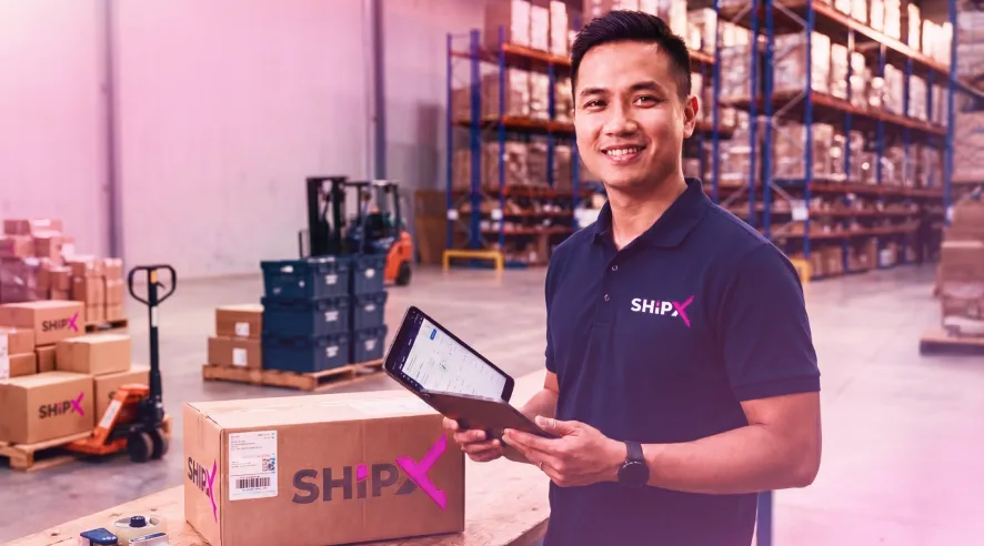 A ShipX team member in the warehouse holding a tablet beside ShipX-branded parcels